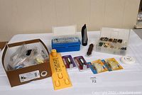 Photo shows a lot with a box containing upholstery tacks, two plastic storage boxes with screws and small hardware, a yellow plastic doorbell stencil, four packaged doorbells, a black handheld flashlight, and other miscellaneous hardware items arranged on a white surface.