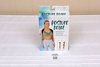 Photo showing the posture brace in its original packaging. The box features a woman wearing the brace, text listing benefits including improved posture and pain relief.