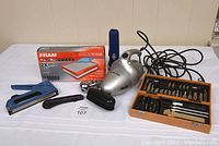 Photo showing Shark handheld vacuum, Fram air filter box, blue staple gun, handheld flashlight, and craft carving set in wooden box