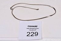 Photo showing the entire 18 inch silver flat snake chain necklace laid flat on a white surface with auction lot number 229 visible.
