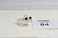 Clear Swarovski crystal frog figurine displayed on white surface with auction tag number 84