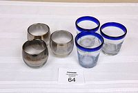 Photo showing two sets of glasses side by side on a white surface. One set is round glasses with smokey edges, the other set is glasses with blue rims.