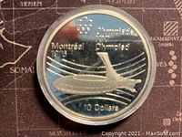 Obverse of the coin shows the 1976 Montreal Olympic stadium design with text 'Montreal 1976', Olympic rings, 'Olympiade' and denomination of '10 Dollars'. The coin is enclosed in a clear protective capsule.