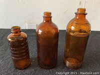 Three vintage amber bottles, varying sizes on black surface, well lit.