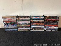 Front view of 60 DVD movie cases stacked in 4 rows on a black floor against a white wall.