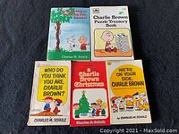 Five vintage Charlie Brown books laid out showing colorful front covers with characters Snoopy, Charlie Brown, and others.