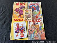 Five vintage Mad Magazines and one small book arranged on dark fabric background showing front cover art and titles