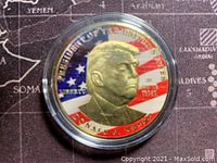 Obverse side showing a relief portrait of Donald Trump with the American flag in the background, detailed and colorful, encased in clear capsule.
