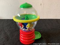 Side view of M&M's spinning candy dispenser showing red spiral base, clear globe with M&M's characters and yellow rim, green lid and green candy chute