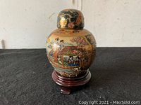 Small round Asian-style ceramic vase with lid, showing side with traditional painted scene of people and flowers on a dark background with gold accents.