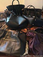 Photo showing multiple black handbags and tote bags of various sizes, stacked closely together
