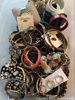 Photo showing a pile of assorted bracelets and earrings, colorful bangles with rhinestones, flower-shaped designs, and metallic bracelets with faux stones.