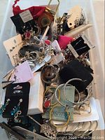 Top view of a plastic container filled with assorted costume jewelry mostly earrings and bracelets on cards