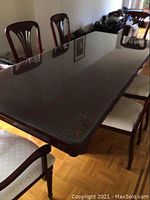 Dark wood rectangular dining table with a glass overlay showing surface reflections and part of the leaf insert extending the table length. Table legs are visible, and floor is parquet.