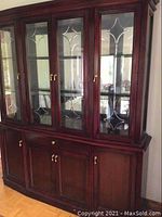 Front and partial side view of large wooden display cabinet showing glass doors with etched designs and lower cabinetry with metal handles
