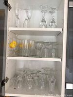 Three shelves of various clear glassware including wine glasses, cocktail glasses, and short glasses.