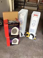 Two Honeywell white oil-filled heaters about 24 inches tall with power cords and control dials, alongside two boxed Rossi portable fan heaters in red and black packaging
