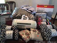 Full lot on table showing throws, linens, pillow, comforter and air mattress box