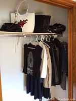 Clothing hung on hangers on a closet rod under a shelf with bags