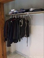 Closet rod with eight clothing items hanging, primarily in dark colors including the fur-trimmed vest at the end.