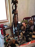 Wide view of lot showing tall carved wooden woman statue, assorted animal figurines, framed artwork, and decorative items.