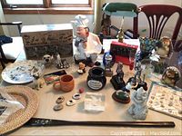 Overview of various decorative items on table including figurines, boxed ceramic zebra espresso cup sets, plates, jar, lamp, and mats.