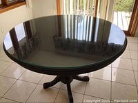 Top view of the round wooden table with thick glass overlay, showing reflective surface and part of the wooden base.