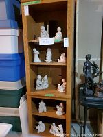 Photo of eleven Austin statues arranged on wooden shelves, with a label stating 'Austin Statues'. Statues are light-colored mostly depicting children in various poses including sitting and playing with toys.