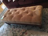 Full view of rectangular tufted bench showing brown fabric upholstery and wooden frame, placed on carpet in living room.