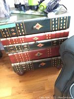 Front view of four-drawer dresser in book spine design on hardwood floor next to upholstered chair.