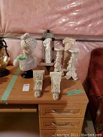 Stone bust of a lady, two decorative wall sconces brackets, two carved candle holders, and a carved wall plaque arranged on wooden desk.