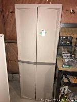 Front view of the beige plastic two door cabinet with label attached on the front.