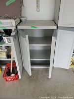 Gray plastic cabinet with both doors open showing two shelves inside. Located next to other storage units, the cabinet interior appears clean and usable.