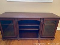 Front view of wood media cabinet showing the two glass doors and central shelving.