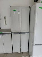 Front view of closed gray plastic double door cabinet adjacent to other cabinets and refrigerator.