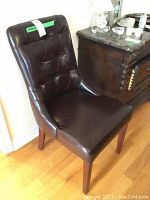 Full side view of the tufted brown leather chair showing the curved back and wooden legs.