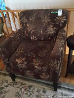 Front view of the brown floral upholstered arm chair with visible floral pattern and angled wooden legs.
