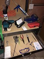Overview showing drill, blue metal vice, caulking gun, safety glasses, small tools, and parts organized on workbench and drawer