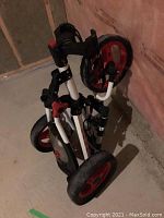 Front view of folded foldable three-wheel golf caddy cart with red rims and black tires.