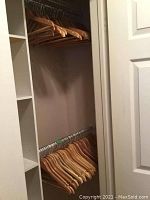 Photo of wooden hangers hanging on a closet rod, showing multiple hangers side by side in natural wood finish.