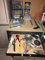 Top shelf with plastic hardware storage cases containing small parts and several small containers with assorted hardware pieces and fasteners.