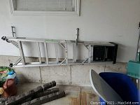 Aluminum five-step ladder placed horizontally inside a garage space, showing full length and condition.