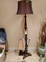 Tall floor lamp with ornate dark metal base and brown shade, showing full height and size of lamp.