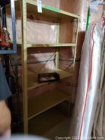 Metal shelving unit with four shelves, beige/tan color, standing in basement with plastic insulation background and nearby items.
