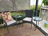 Photo showing two resin woven armchairs with light beige cushions and decorative red floral cushion on one chair. Two metal framed side tables with clear glass tops and decorative curled legs also shown.