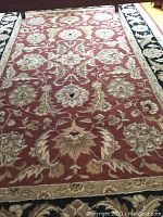 Full view of the handmade oriental Persian romance rug showing the red floral center and black bordered edge.
