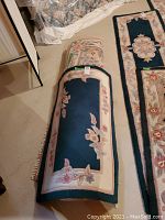 Rolled and flat view of two area rugs showing floral border pattern on dark center background