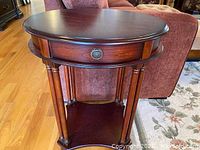 Side view of the round wooden table showing drawer and lower shelf with four turned legs.