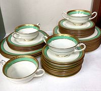 Photo showing multiple stacks of plates and saucers with turquoise and gold trim, including double-handled soup cups stacked on top.