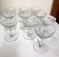 Front view of the 10 crystal glasses arranged loosely on a white surface showing etched starburst floral pattern
